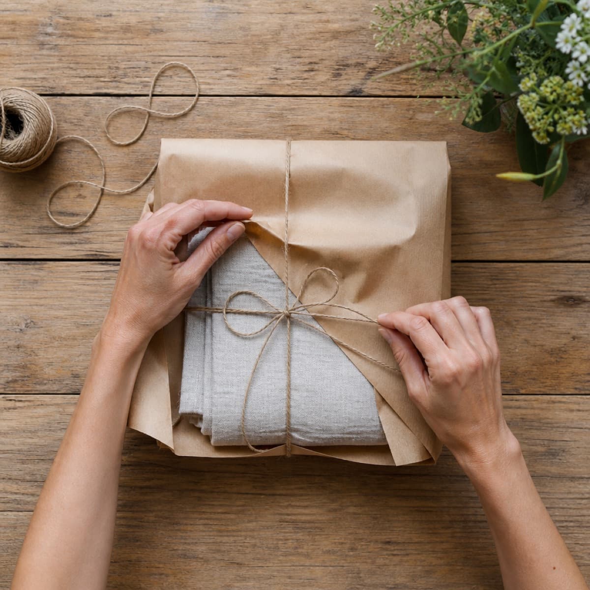 The Instagram picture: hands wrapping a folded linen bundle in brown paper on a wooden table